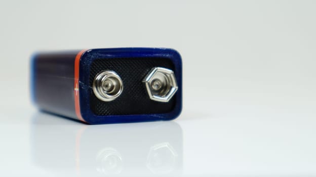One blue used PP3 battery on a white background with reflection. Main battery for personal power supplies. Close-up of a scratched and used battery connector