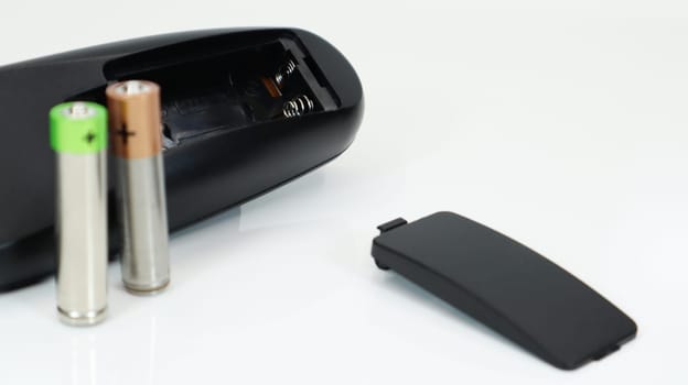 Black TV remote control with AAA alkaline batteries on a white background. Battery replacement, spare parts. Close up of an empty battery compartment of the remote control