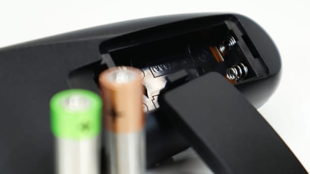 Black TV remote control with AAA alkaline batteries on a white background. Battery replacement, spare parts. Close up of an empty battery compartment of the remote control