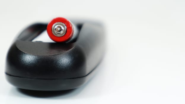 Black TV remote control with AAA alkaline batteries on a white background. Battery replacement, spare parts. Close up of the battery compartment of the remote control
