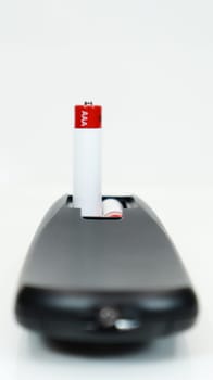 Black TV remote control with AAA alkaline batteries on a white background. Battery replacement, spare parts. Close up of the battery compartment of the remote control. Vertical photography