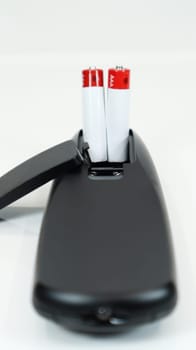 Black TV remote control with AAA alkaline batteries on a white background. Battery replacement, spare parts. Close up of the battery compartment of the remote control. Vertical photography