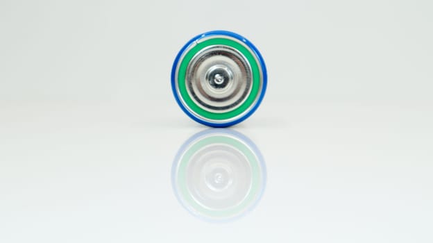 Large battery type D or C cell on white background with reflection. View of a metallic alkaline battery with copy space. Mandatory processing