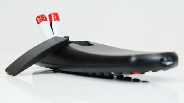 Black TV remote control with AAA alkaline batteries on a white background. Battery replacement, spare parts. Close up of the battery compartment of the remote control
