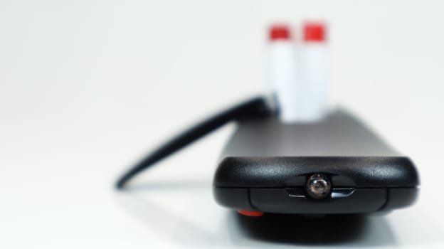 Black TV remote control with AAA alkaline batteries on a white background. Battery replacement, spare parts. Close up of the battery compartment of the remote control