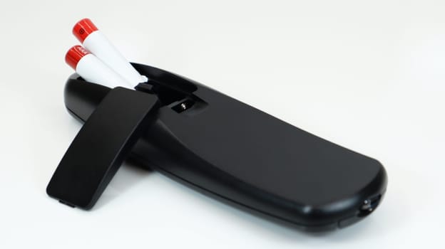 Black TV remote control with AAA alkaline batteries on a white background. Battery replacement, spare parts. Close up of the battery compartment of the remote control