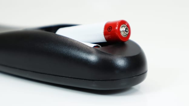Black TV remote control with AAA alkaline batteries on a white background. Battery replacement, spare parts. Close up of the battery compartment of the remote control