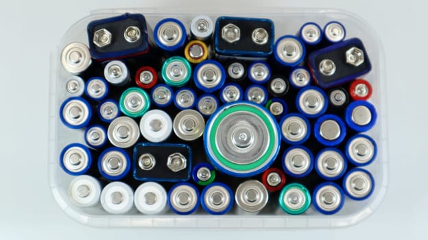Clear plastic box full of used household AA alkaline and lithium-ion batteries collected for recycling in special waste bins. Recycling and ecology problems. View from above.