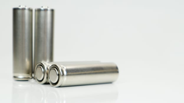 AA alkaline rechargeable batteries on white glossy background with reflection. Close up four empty batteries with copy space