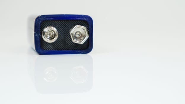 One blue used PP3 battery on a white background with reflection. Main battery for personal power supplies. Close-up of a scratched and used battery connector