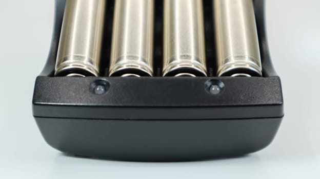 Rechargeable alkaline batteries in a battery charger on a white background. AA fast charger in black. The battery is charging