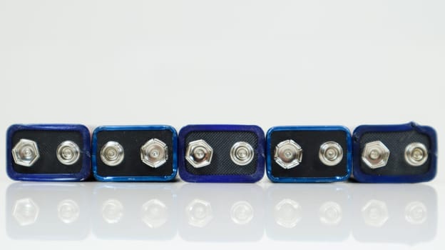 Five blue used PP3 batteries lined up on a white background with reflection. Main battery for personal power supplies. Close-up of a scratched and used battery connector