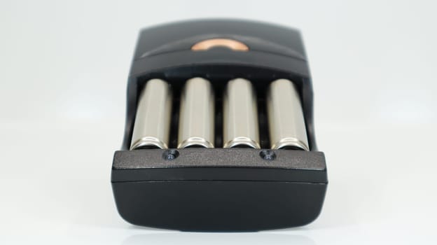 Rechargeable alkaline batteries in a battery charger on a white background. AA fast charger in black. The battery is charging