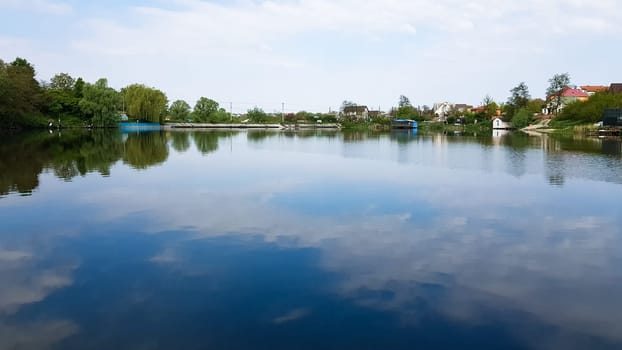 Cumulus clouds and sky are reflected in the lake water on a sunny summer day. Beautiful natural landscape