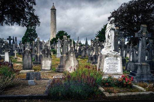 Dublin, Ireland, August 2019 Ancient graves and tombstones in Glasnevin Cemetery with Round Tower in background