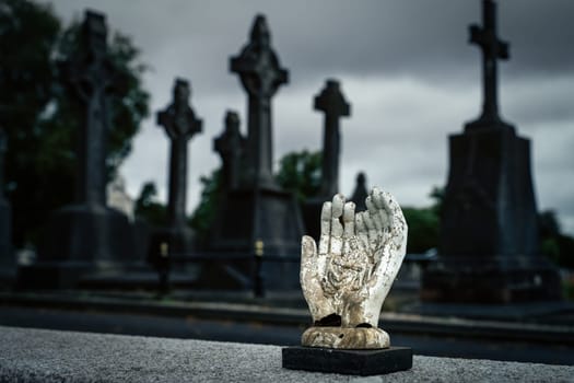 Dublin, Ireland, August 2019 Sculpture of hands holding holly Mary and Jesus Christ with blurred Celtic crosses in Glasnevin Cemetery