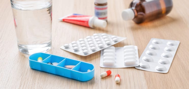 Different medicine pills and capsules with blister packs and a glass of water