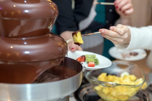Vibrant chocolate fountain on wedding party. Chocolate fondue with fruits.