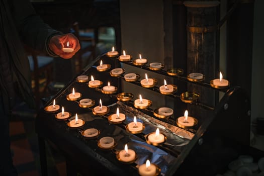 Hand holding a lit candle, putting it on altar. Candles are lit for prayer intentions in places of worship. St Patricks Cathedral, Dublin, Ireland