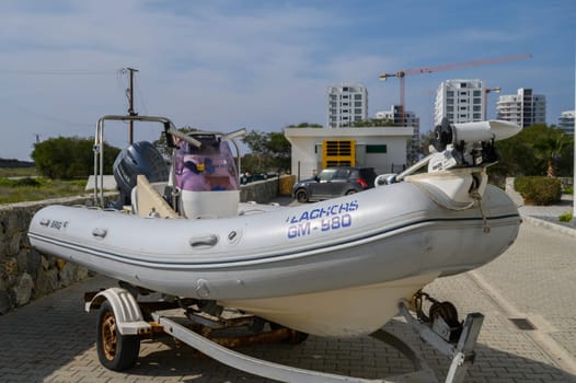 Gaziveren Cyprus -15.02.2025 A small inflatable boat rests on a trailer by the waterfront under a bright sky, surrounded by modern buildings.