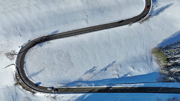 Aerial drone shot of snowy landscape with curvy road with cars