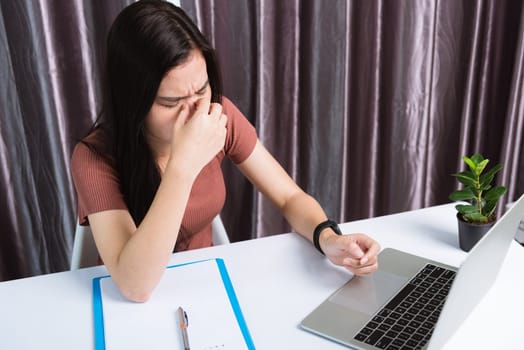 Work from home, Fatigued or strain Asian business young beautiful woman sits on desk workspace feeling tired stressed hold his nose close eyes after see screen long time of laptop computer at office