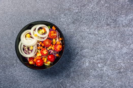 Top view of the healthy colorful salad bowl with tomatoes fresh mixed leaves vegetable in a dish on cement stone table background, Health salad snack diet food weight loss concept