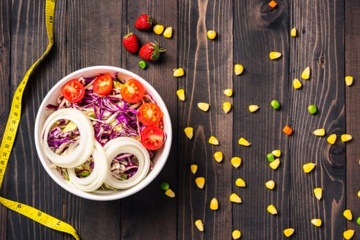 Top view of the healthy colorful salad bowl with tomatoes fresh mixed greens vegetable in a dish and measuring tape on black wooden background, Health salad snack diet food weight loss concept