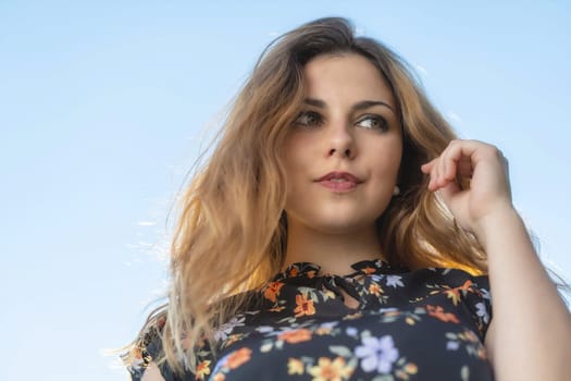 Atractive long haired young woman is posing outdoors against blue sky.