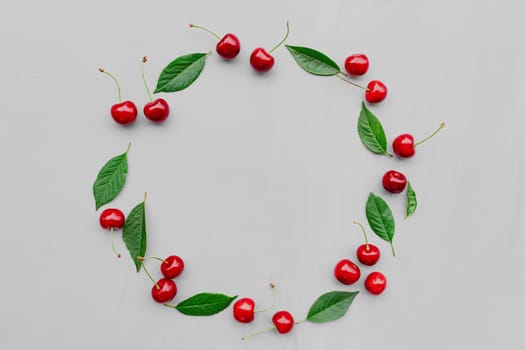 Gray concrete flat lay with big sweet cherries on table background. Top view on huge, massive organic cherry berries with leaves in form of empty circle shape. Copy space area for advertisement text