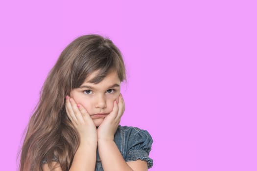 Sad tanned long haired little girl wears  denim costume is posing on pink  background.