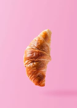 Freshly baked croissant levitating or flying. Croissant fly in the air isolated on pink background. Levitation scene. Copy space place for text. Signboard mockup. Creative breakfast food