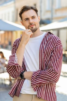 Sad unhappy bearded man thinks over life concerns, suffers from unfair situation. Problem, feeling bad annoyed, burnout grief. Frustrated depressed lonely young guy standing in city street. Vertical