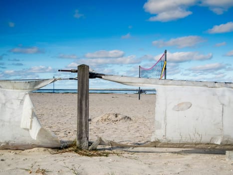 Scene on the beach of Bensersiel in northern Germany with a broken fence in front of a beach volleyball court in front of a blue sky with small clouds.