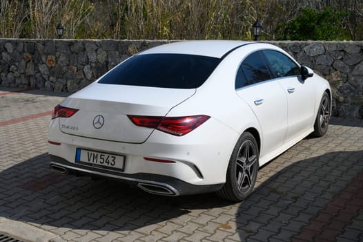 Gaziveren Cyprus -15.02.2025 Modern sedan gleams in the sunlight, showcasing its elegant design while parked beside a rugged stone wall.