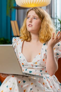 Displeased woman use laptop notebook typing browsing working, loses becoming surprised sudden lottery results bad news fortune loss fail computer virus. Redhead girl at home in room on couch. Vertical