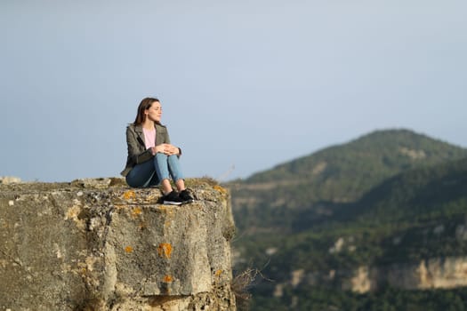 Casual woman sitting contemplating views from the top of a cliff in the mountain