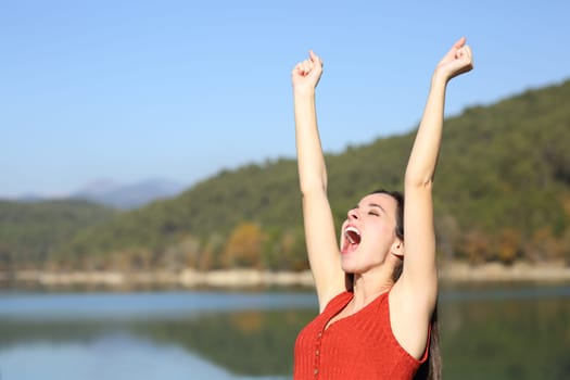 Euphoric woman celebrating vacation raising arms in summer in a lake