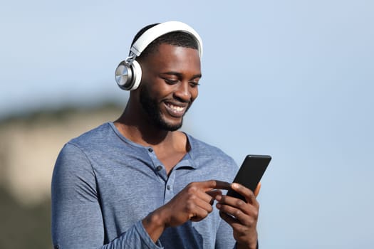 Happy man with black skinwearing wireless headphones listening to music on smart phone outdoors