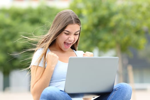 Excited teen checking good news on laptop in the street