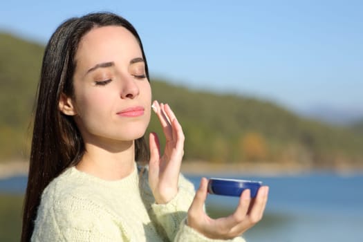 Woman applying moisturizer cream on face in a lake in winter
