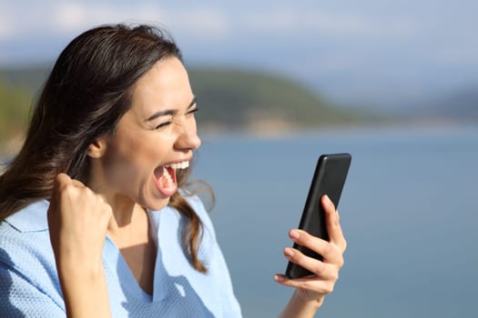 Excited woman in a lake checking smart phone on vacation