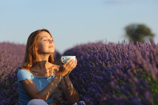 Happy woman relaxing drinking coffee in lavender field at sunset