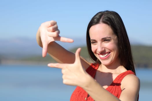 Happy woman in red framing gesturing with hands in a lake on vacation