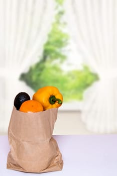 Closeup of a brown paper shopping bag with fresh vegetables on table over blurred abstrract curtain background. Space for product display montage. Concept of strengthening the immune system.