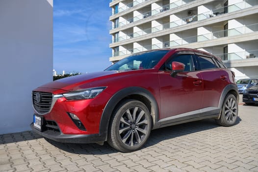 Gaziveren Cyprus -15.02.2025 A striking red crossover vehicle is parked against a backdrop of sleek modern buildings under bright sunlight.