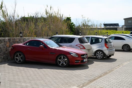 Gaziveren Cyprus -15.02.2025 A striking red sports car is nestled between smaller cars, basking in the warm sunlight of a beautiful day.
