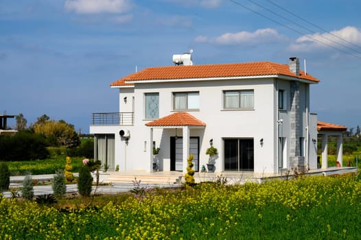 Bright, spacious home nestled in lush greenery and vibrant flowers under a clear blue sky on a warm day.