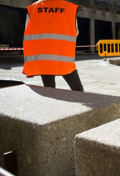 Staff worker watching security area marked by mobile fence and cones and tape