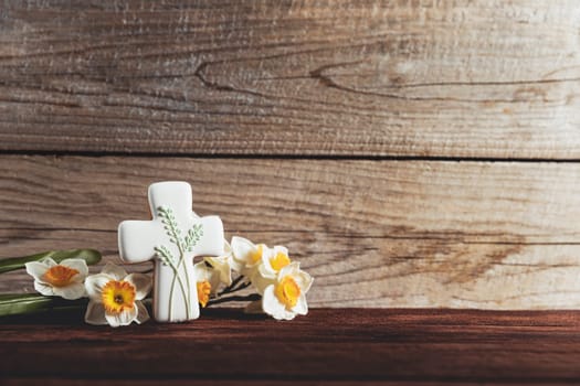 Easter holiday conceptual background on rustic wooden boards. Photo of gingerbread cookie Cross shape, narcissus or daffodils flowers on table top. Card with copy space to place text. Minimal concept